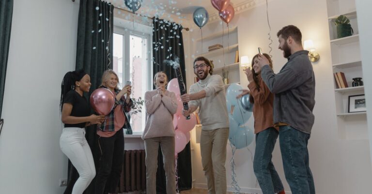 Excited friends celebrate a gender reveal with balloons and confetti indoors.